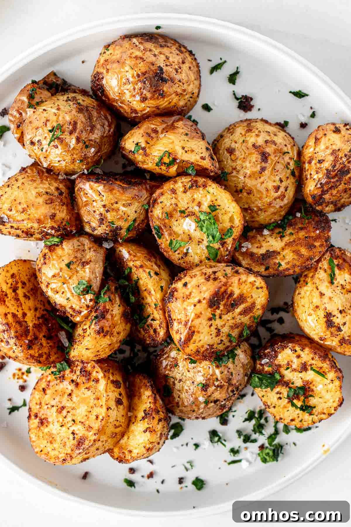 Crispy Air Fryer Potatoes with Garlic and Herbs 3 Air fryer potatoes on a white plate served with fresh parsley.
