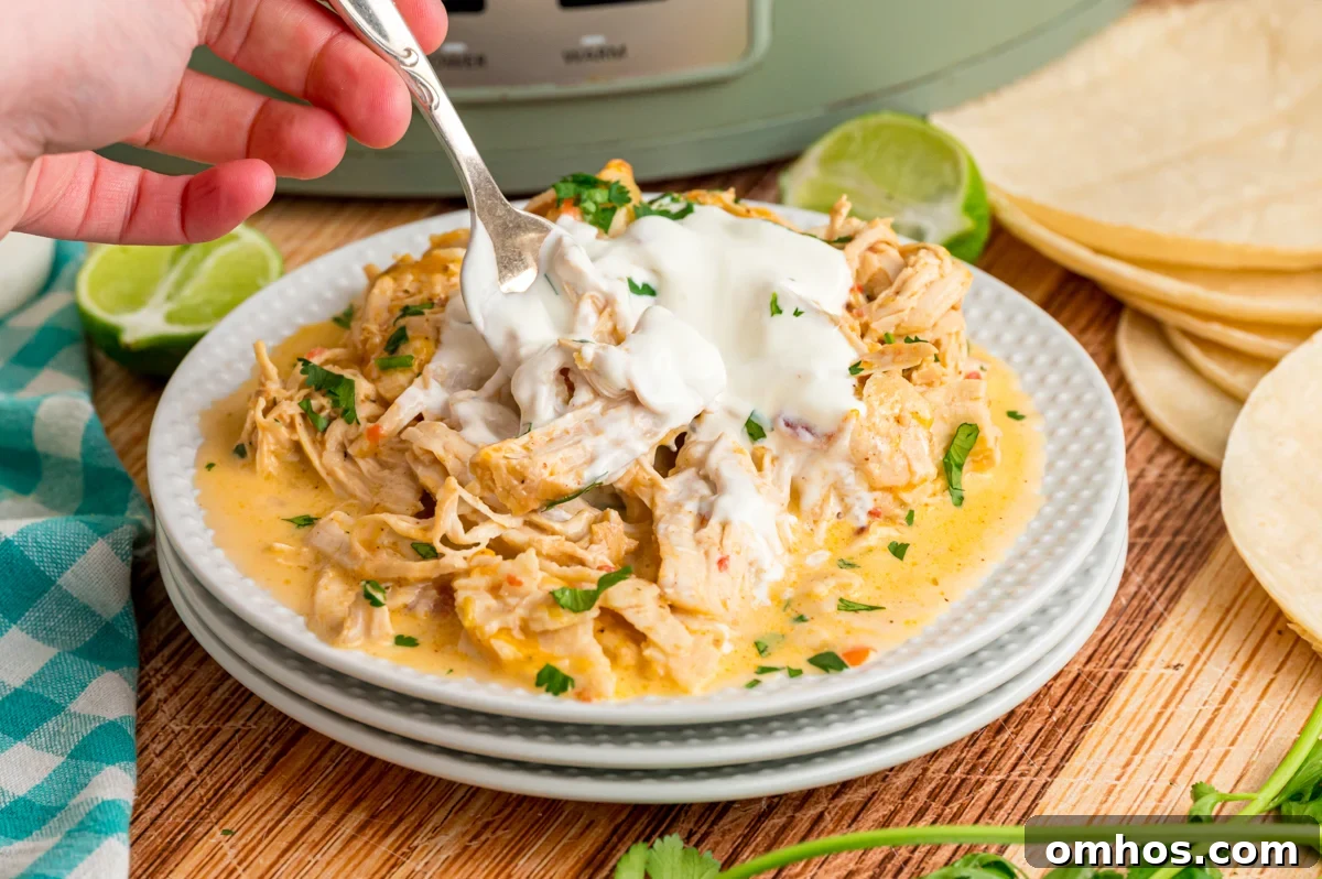 Classic King Ranch Chicken Casserole Recipe 7 A hand holding a fork grabbing some chicken from to top of a stack of white plates.
