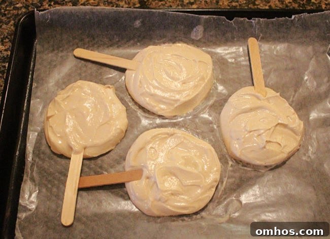 Circles of Greek yogurt with popsicle sticks on a baking sheet.