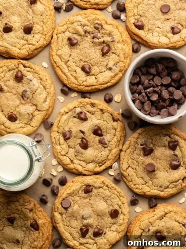 Oat flour chocolate chip cookies on a cookies sheet with a bowl of chocolate chips and a jar of milk.