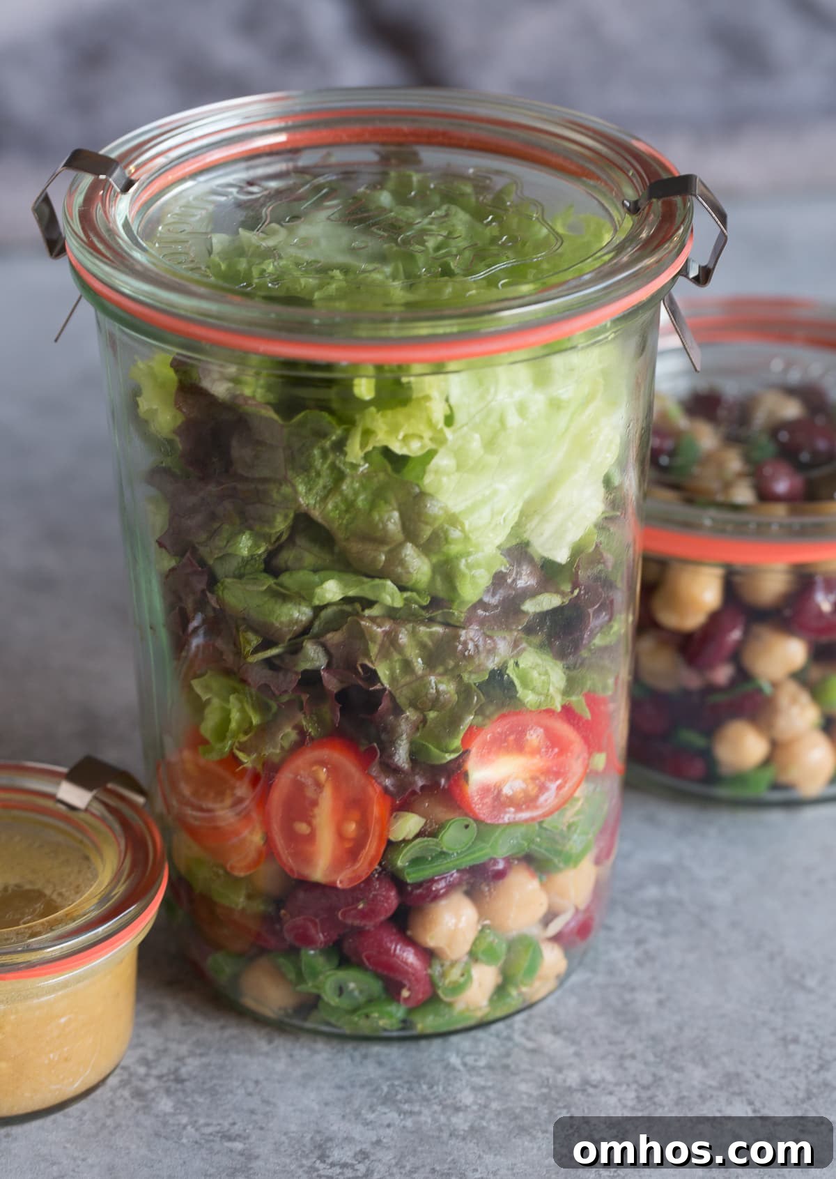 A tall jar of meal prepped bean salad with lettuce, tomatoes and dressing.