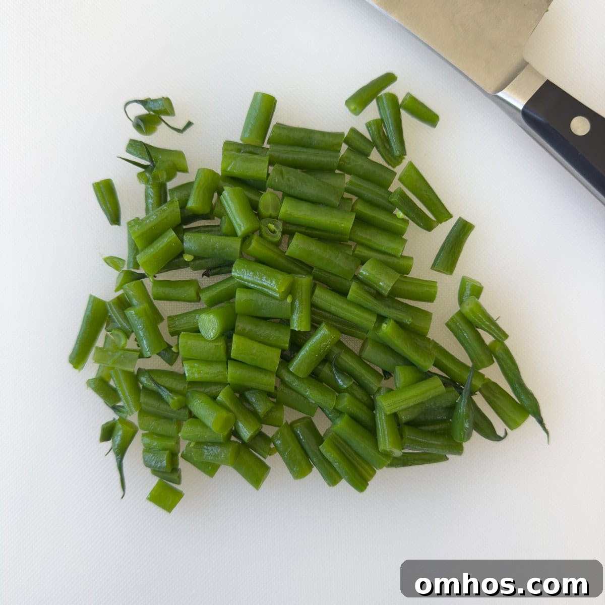 Chopped green beans on a white cutting board with a knife.