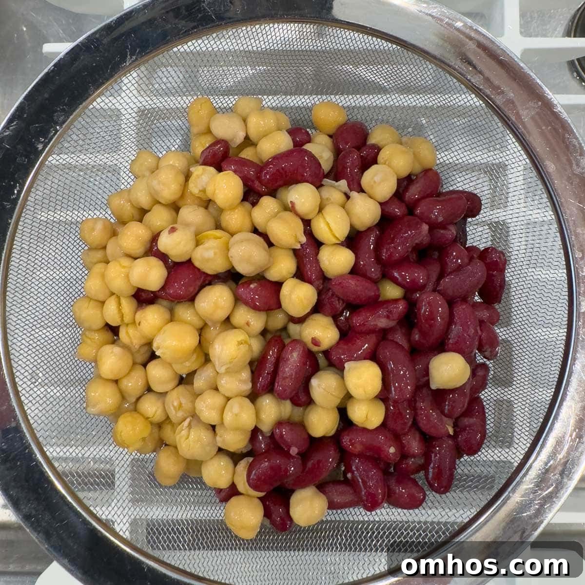 Gold and red beans in a stainless steel sieve draining in the sink.