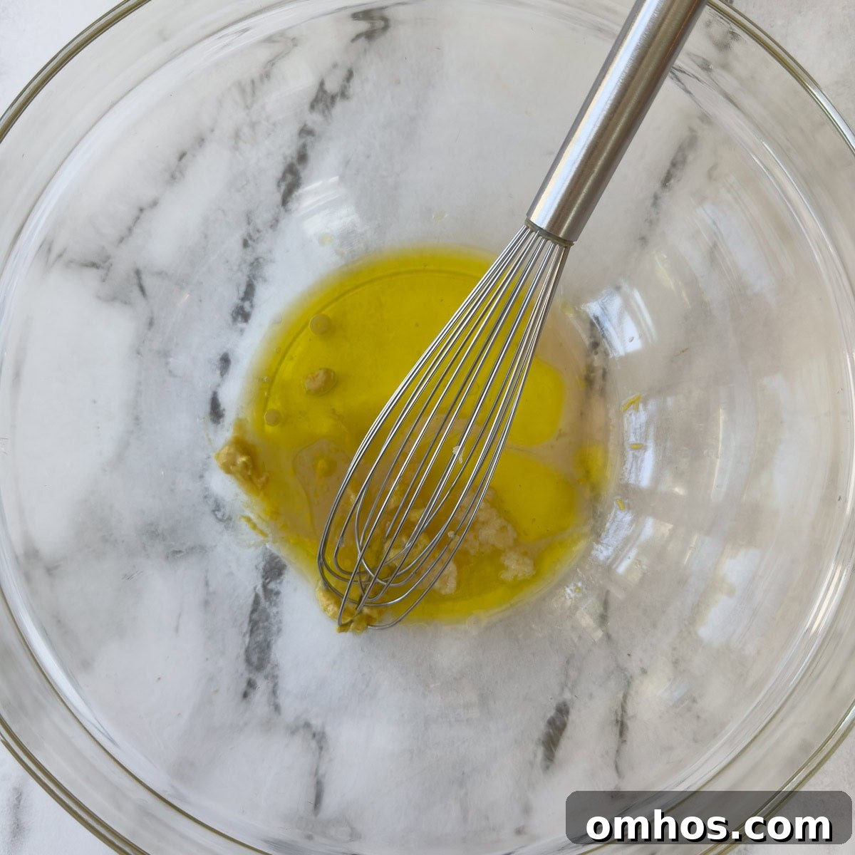 Ingredients for a vinaigrette in a glass bowl with a steel whisk.
