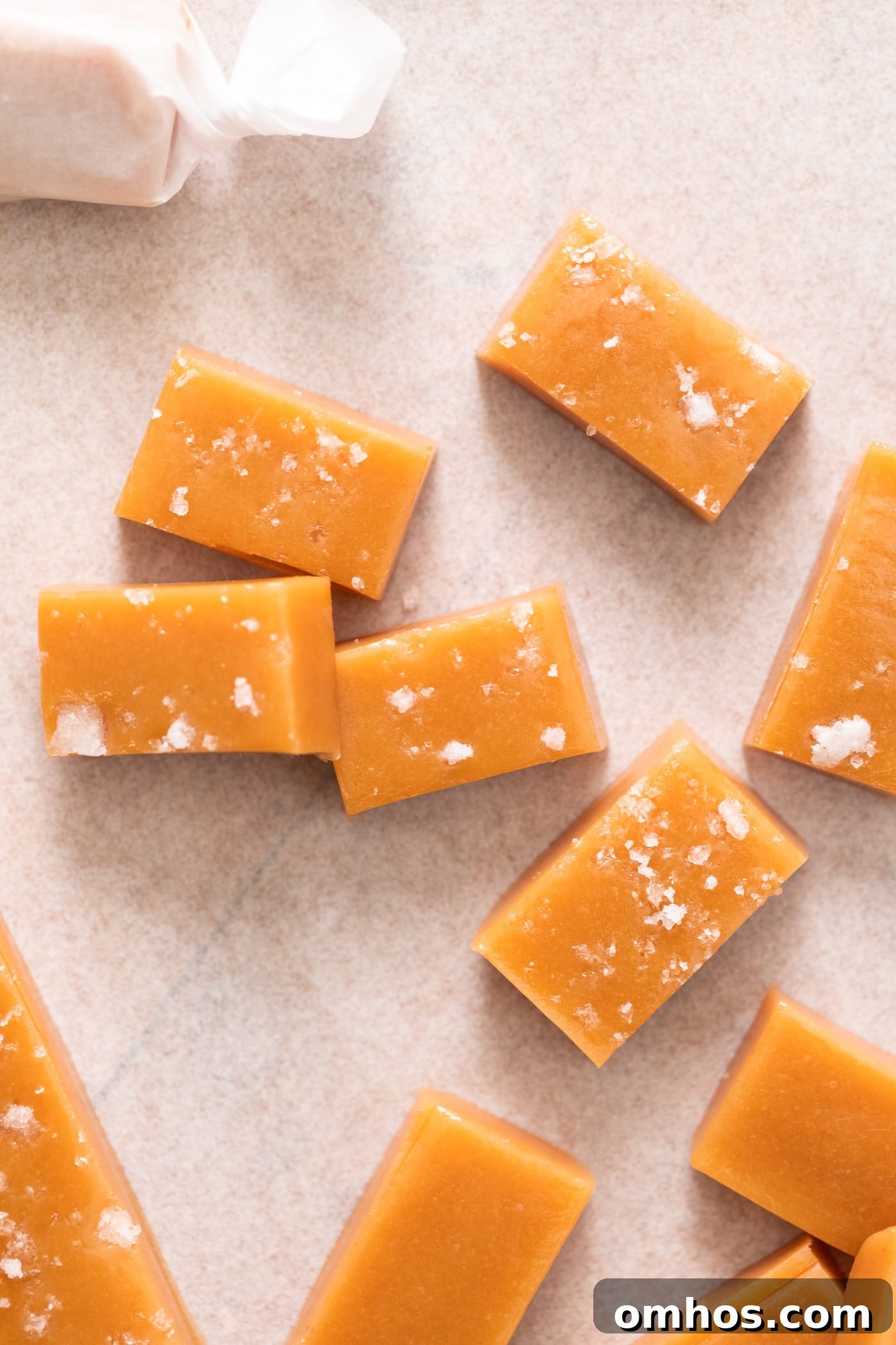 Top down view of pieces of caramel, some with sea salt on top, sitting on white piece of parchment