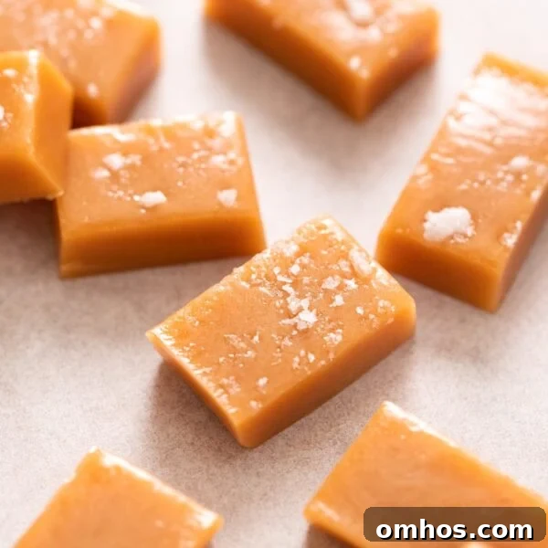 Pieces of golden caramel sitting on white piece of parchment, some topped with flaky sea salt