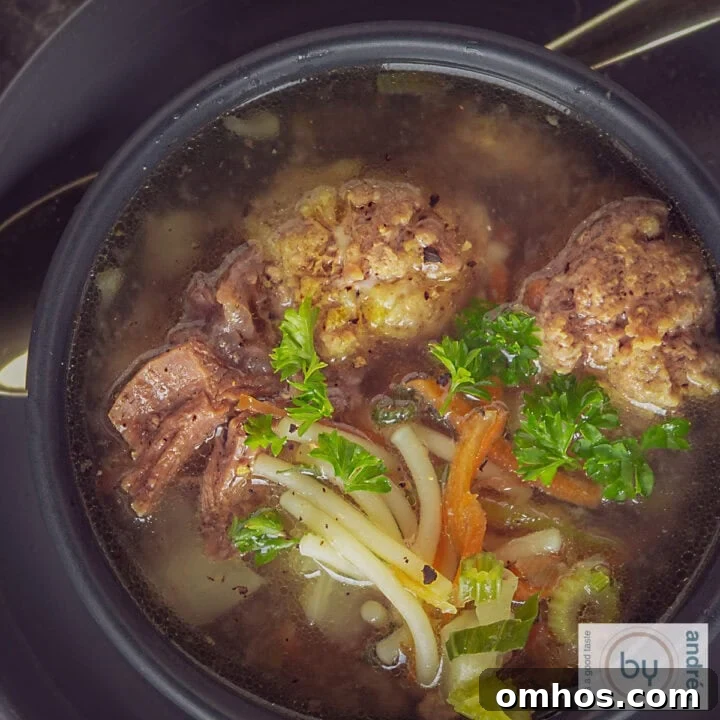 A square photo from above of vegetable soup with meatballs, vegetables, vermicelli and parsley.