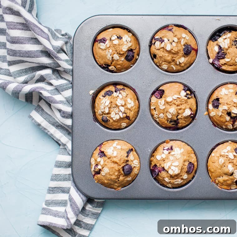 Moist Blueberry Oatmeal Muffins Recipe 4 Golden blueberry muffins on a wooden bread board with blue and white linen.