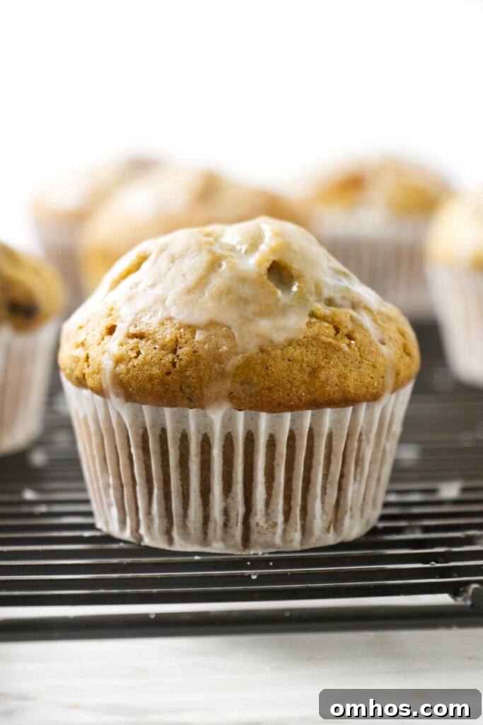 An iced zucchini muffin on a bakers rack with a paper cupcake liner.