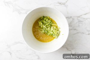 Adding shredded zucchini to the wet ingredients for muffins.