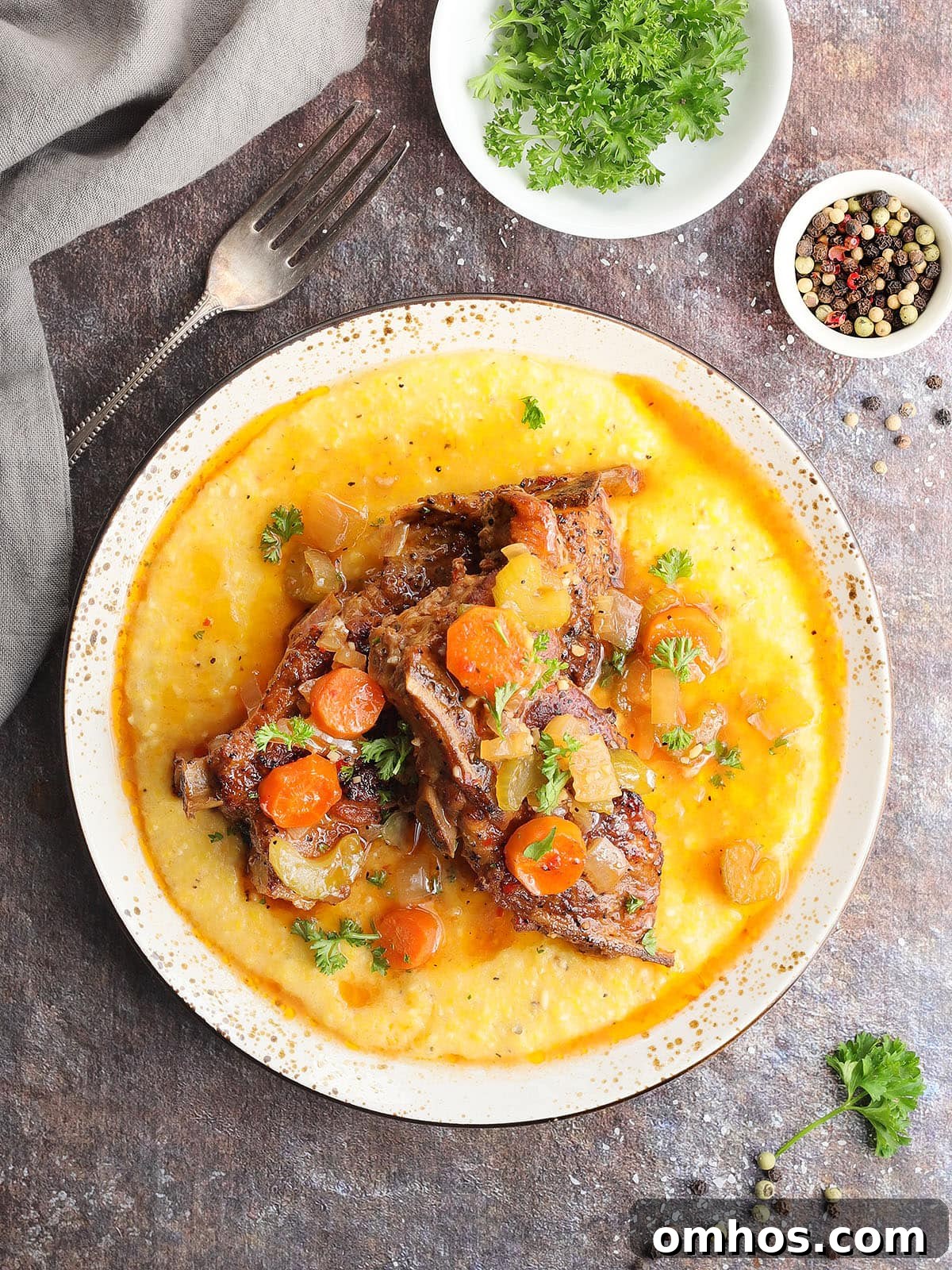 Slow cooker country style pork ribs nestles on a bed of cheese grits and topped with parsley, carrots, onions, and celery.