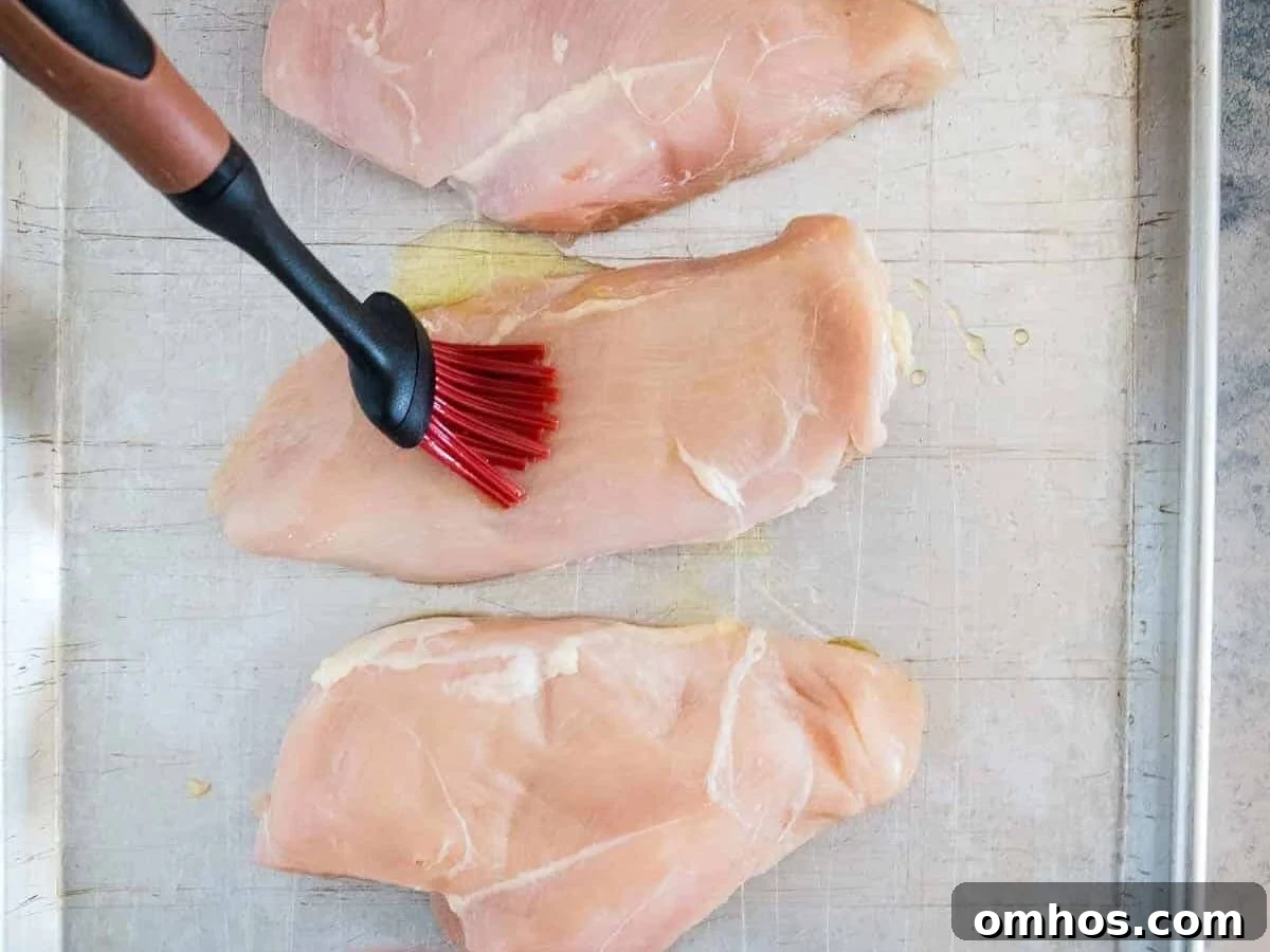 Basting brush putting olive oil on chicken breast