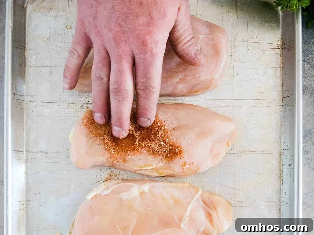 Hand putting seasoning on chicken breast