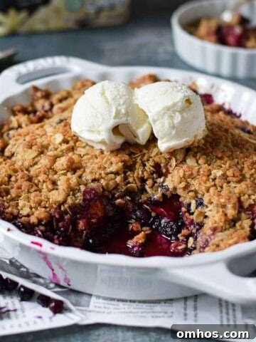 Angled view of blueberry crisp in a white plate with ice cream on top.