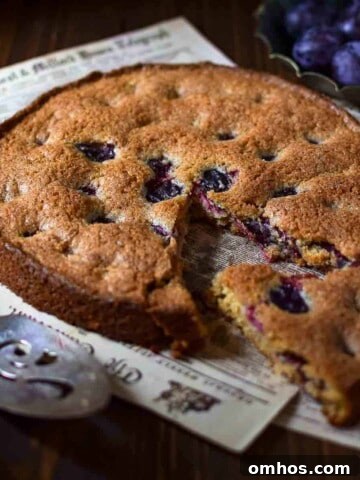 Angled view of plum cake with a slice removed on a wood surface.