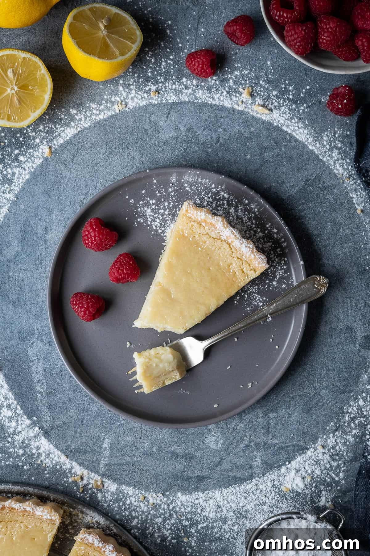 Slice of vegan lemon tart with raspberries A slice of vegan lemon tart with raspberries and a fork on a grey plate