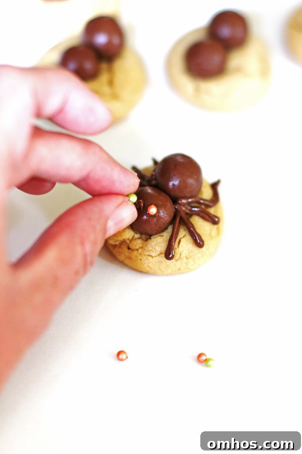 Placing the candy eyes on the spiders that are on top of the cookies.