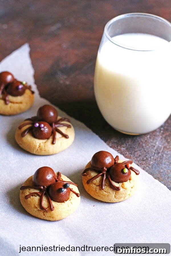 Cookies decorated with candy spiders on top with a glass of milk on a table.