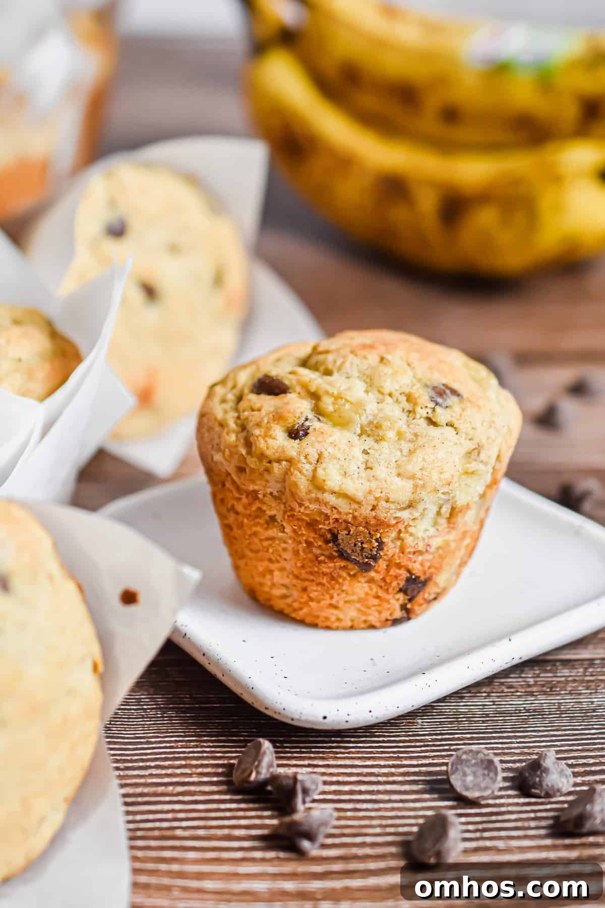 One banana muffin with self-rising flour is on a plate surrounded by other bananas and more muffins