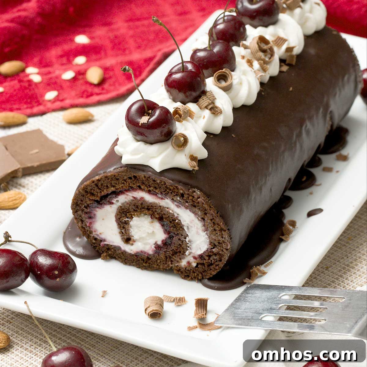 A gluten-free chocolate Swiss roll with cherries and whipped cream on top on a cake pan with a spatula.