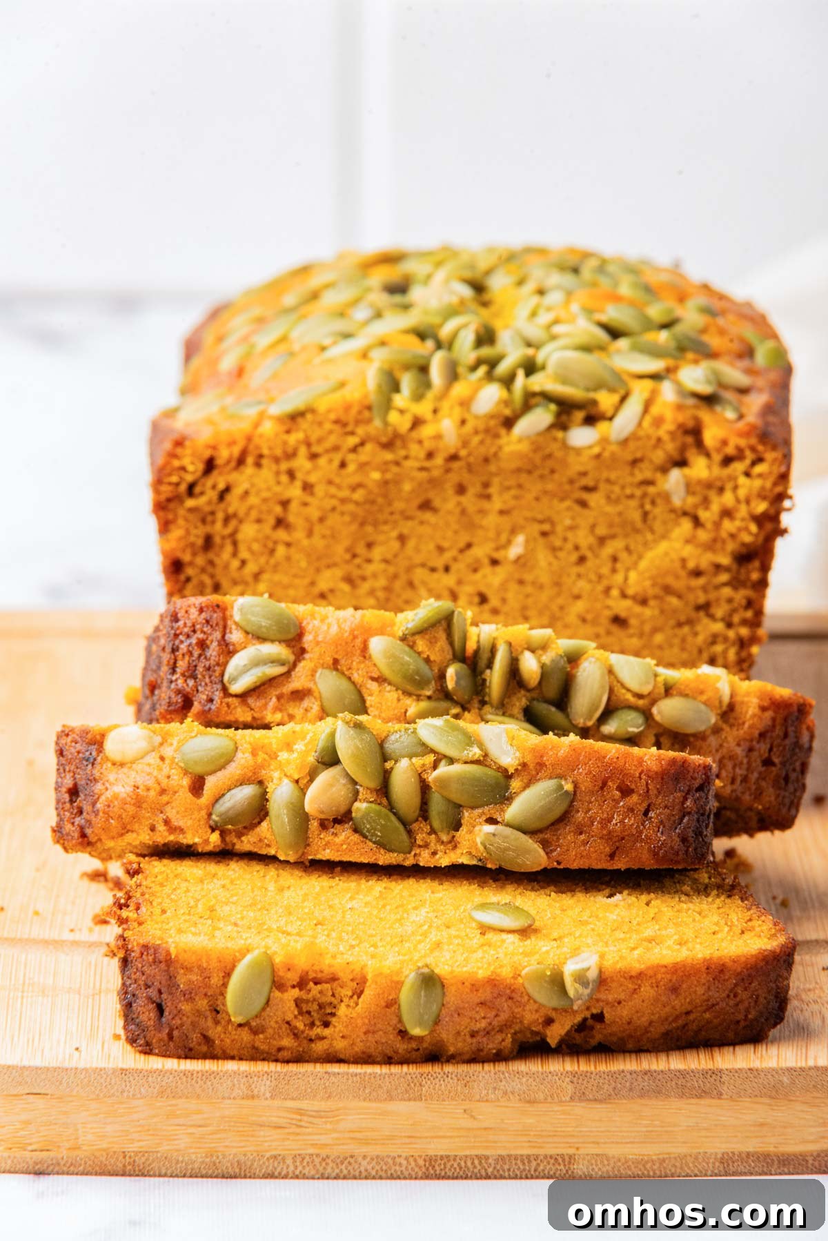 Starbucks-Style Pumpkin Bread Recipe 12 A loaf of pumpkin bread with a few slices cut and arranged in front, showcasing the interior texture and pumpkin seed topping.