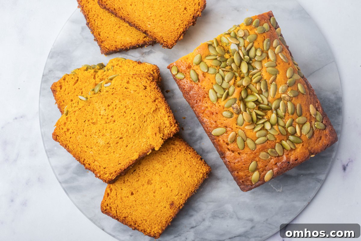 Starbucks-Style Pumpkin Bread Recipe 13 A top-down view of a loaf of pumpkin bread and several slices, displaying the rich orange color and seed topping on a marble surface.