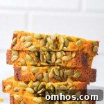 A stack of sliced copycat Starbucks pumpkin bread with a hand picking up the top slice, emphasizing the texture and pumpkin seed topping.