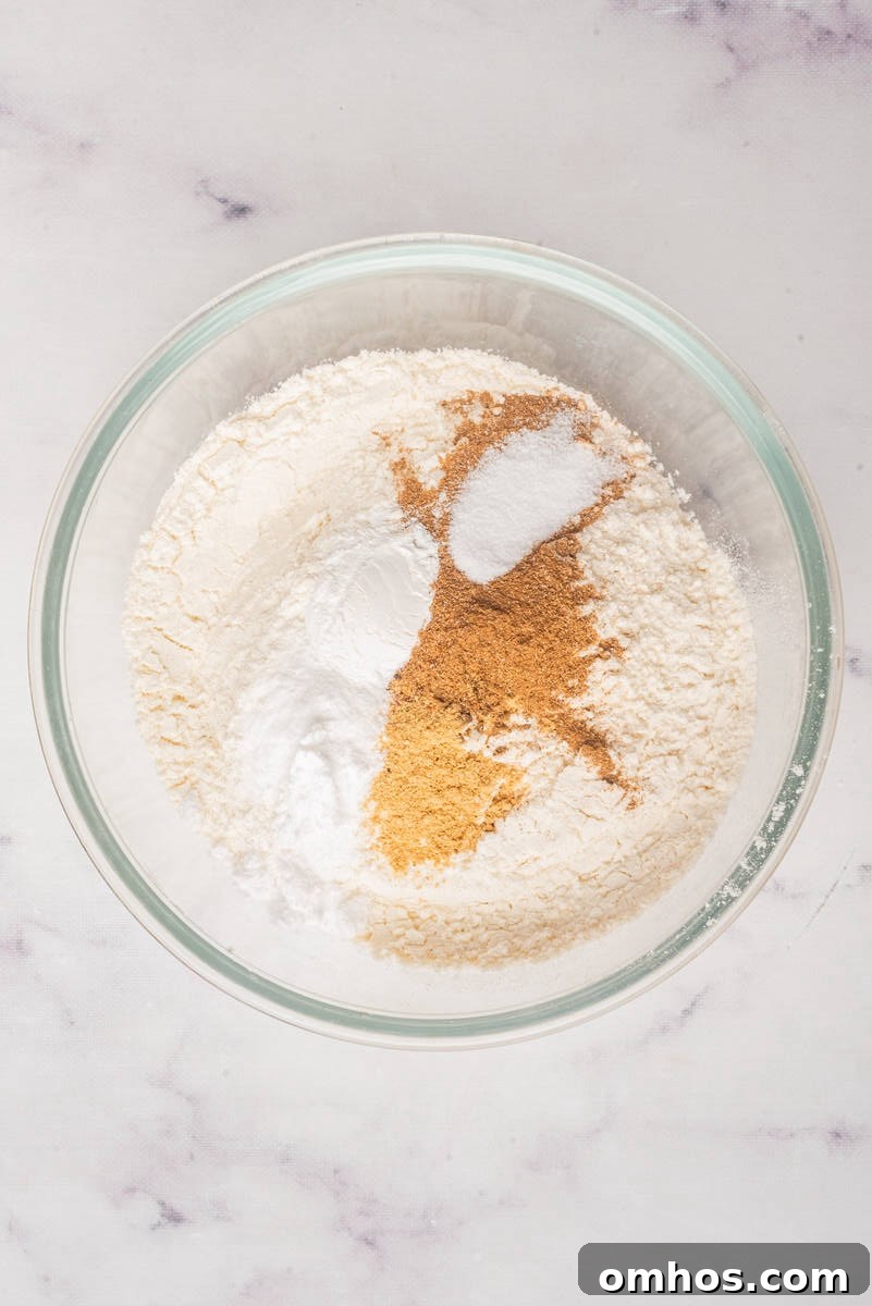 Starbucks-Style Pumpkin Bread Recipe 5 A glass bowl containing dry ingredients for baking, including flour, baking powder, baking soda, salt, and brown spices.