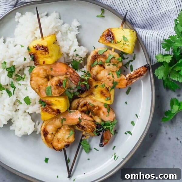 Overhead view of two grilled kabobs on a plate, with shrimp and fresh pineapple.