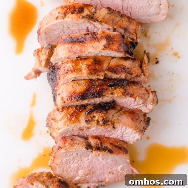Sliced roasted pork tenderloin with a browned crust and juices on a white surface.