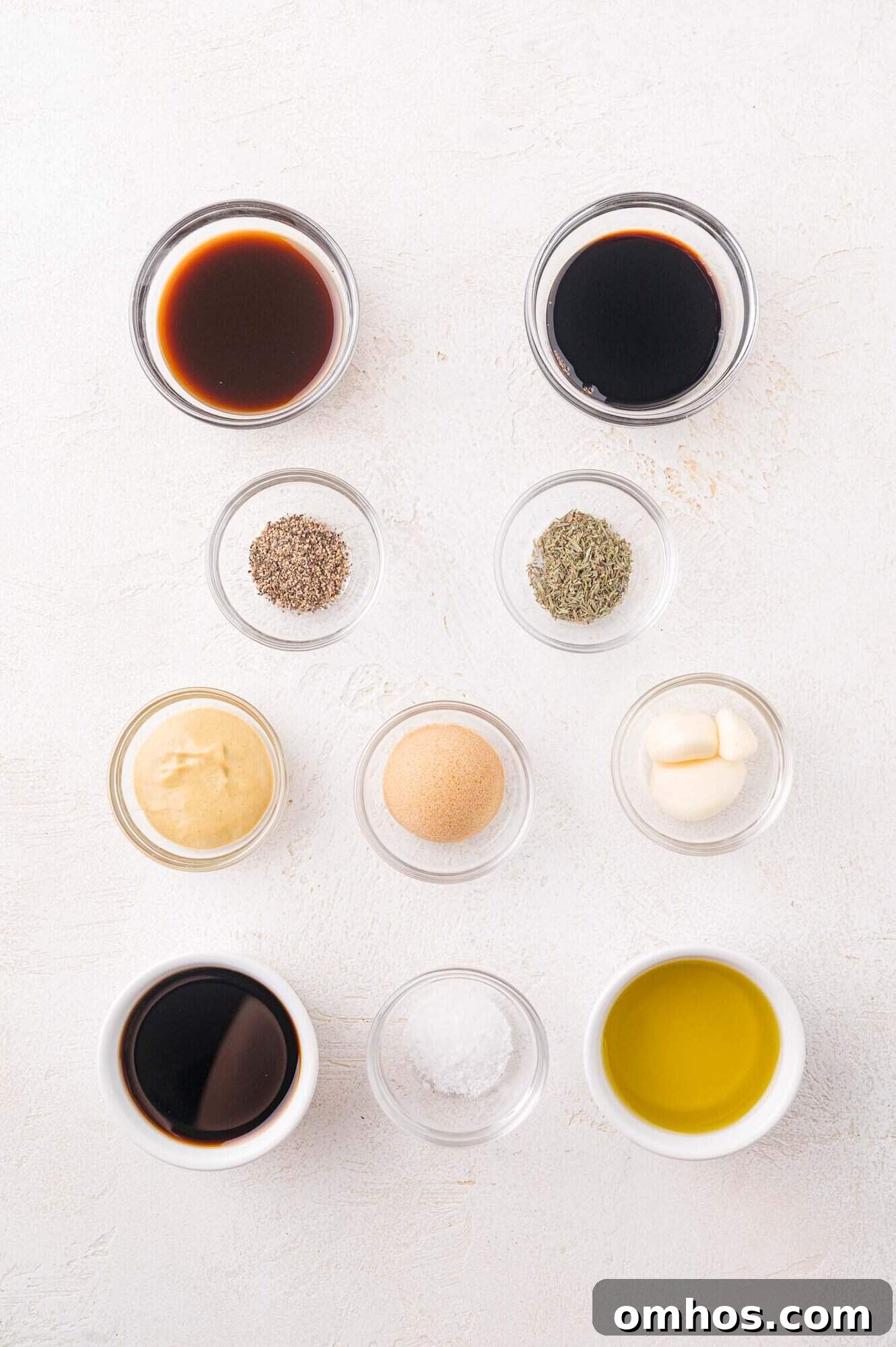 Nine small glass bowls on a white surface, each containing different ingredients.