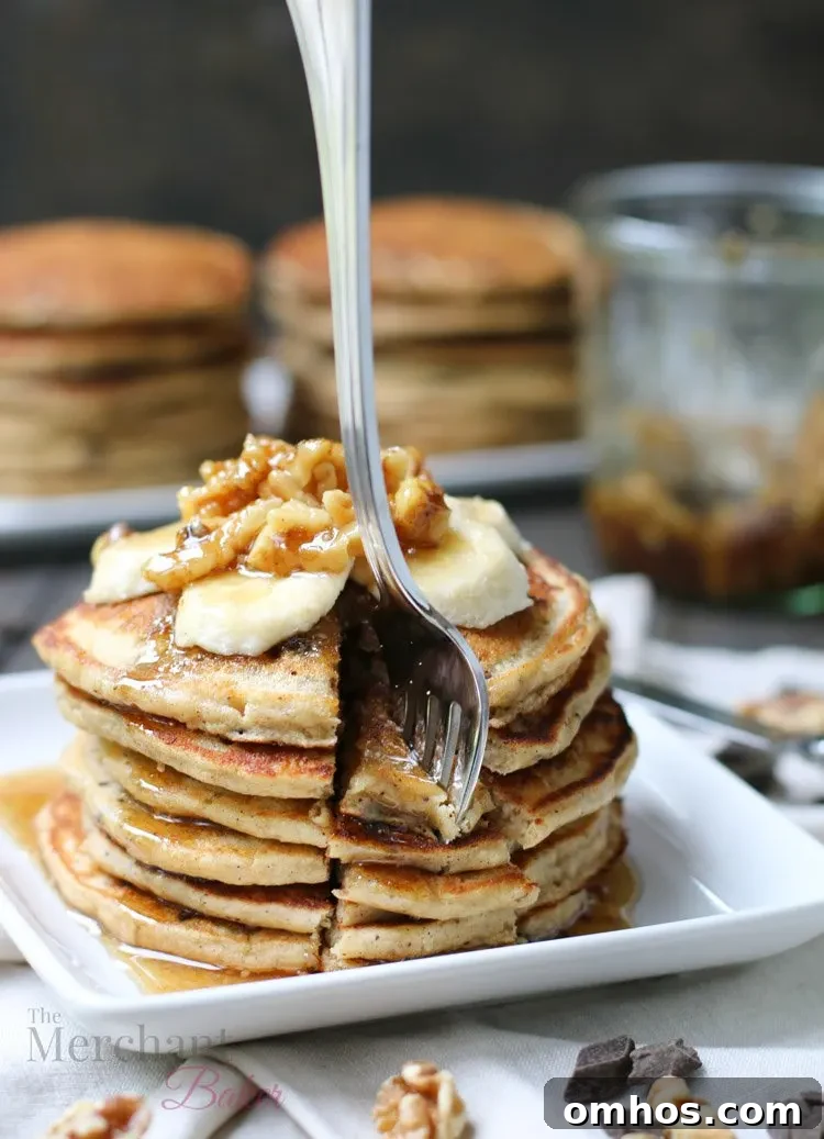 Stack of Oatmeal Chocolate Chip Banana Pancakes speared with a fork topped with sliced bananas and walnut syrup