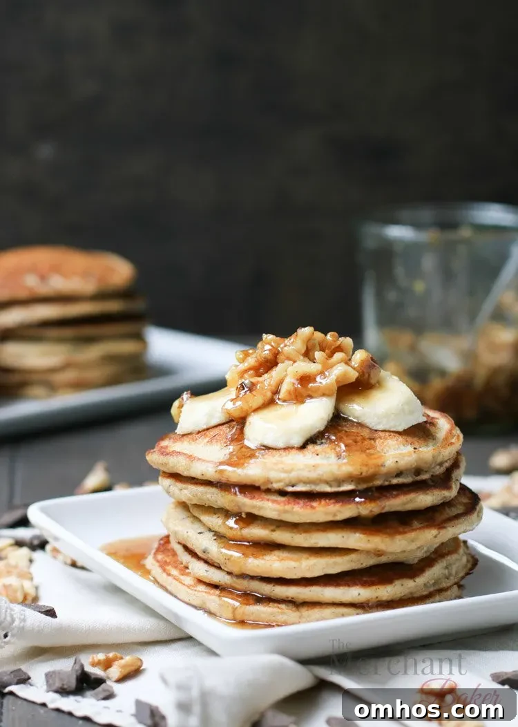 Stack of Oatmeal Chocolate Chip Banana Pancakes topped with sliced bananas and walnut syrup