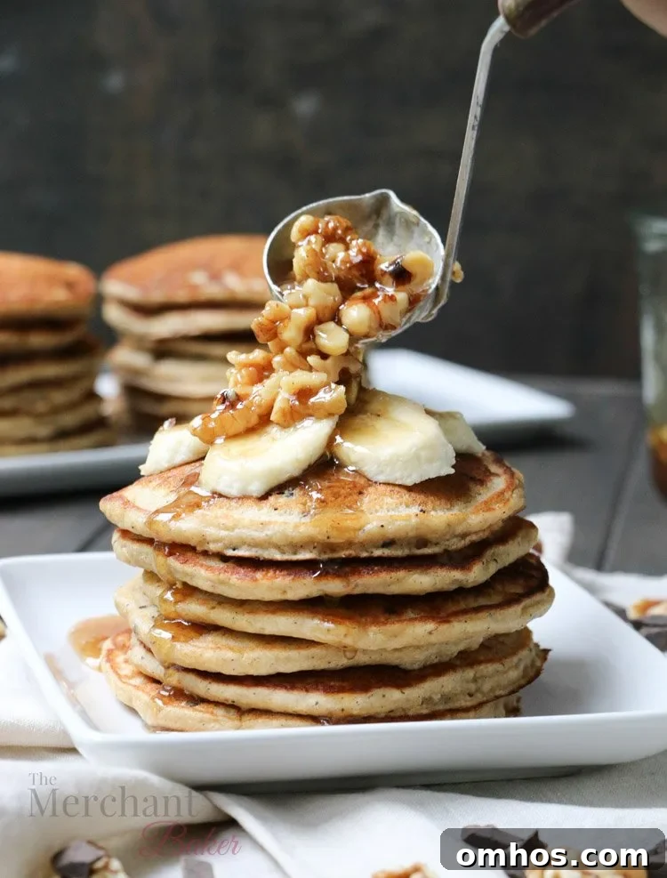 Walnut syrup being ladled over a stack of Oatmeal Chocolate Chip Banana Pancakes topped with sliced bananas