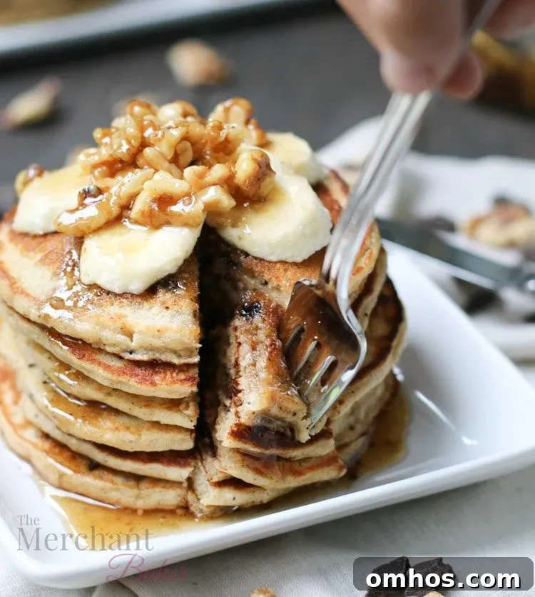 Stack of Oatmeal Chocolate Chip Banana Pancakes speared with a fork topped with sliced bananas and walnut syrup