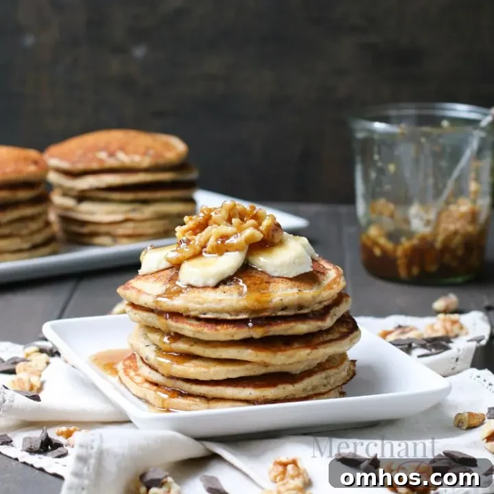 Stack of Oatmeal Chocolate Chip Banana Pancakes topped with sliced bananas and walnut syrup from themerchantbaker.com