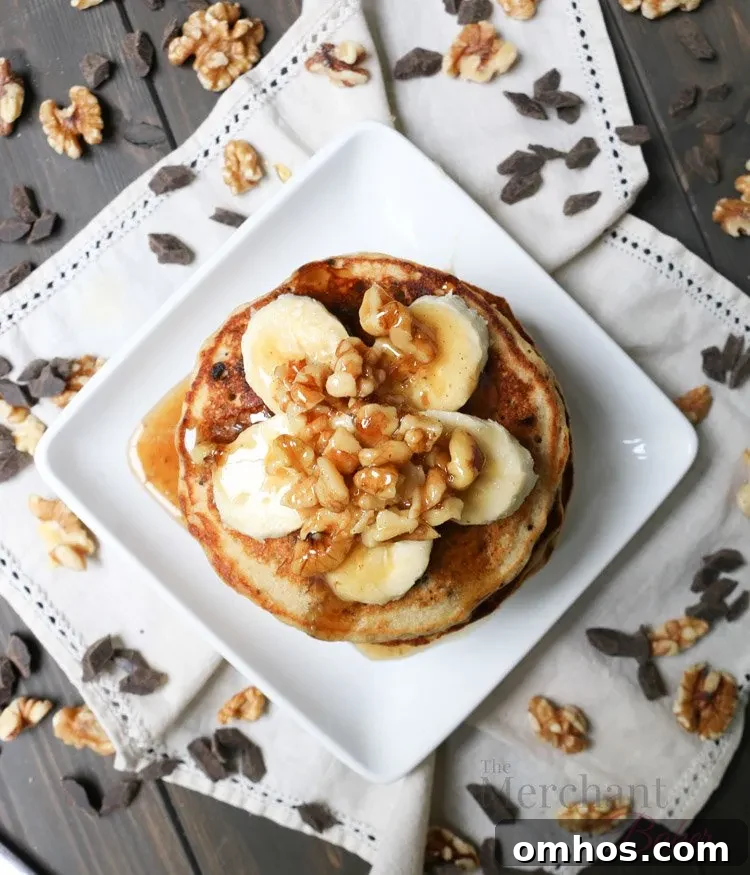 Overhead view of Stack of Oatmeal Chocolate Chip Banana Pancakes topped with sliced bananas and walnut syrup