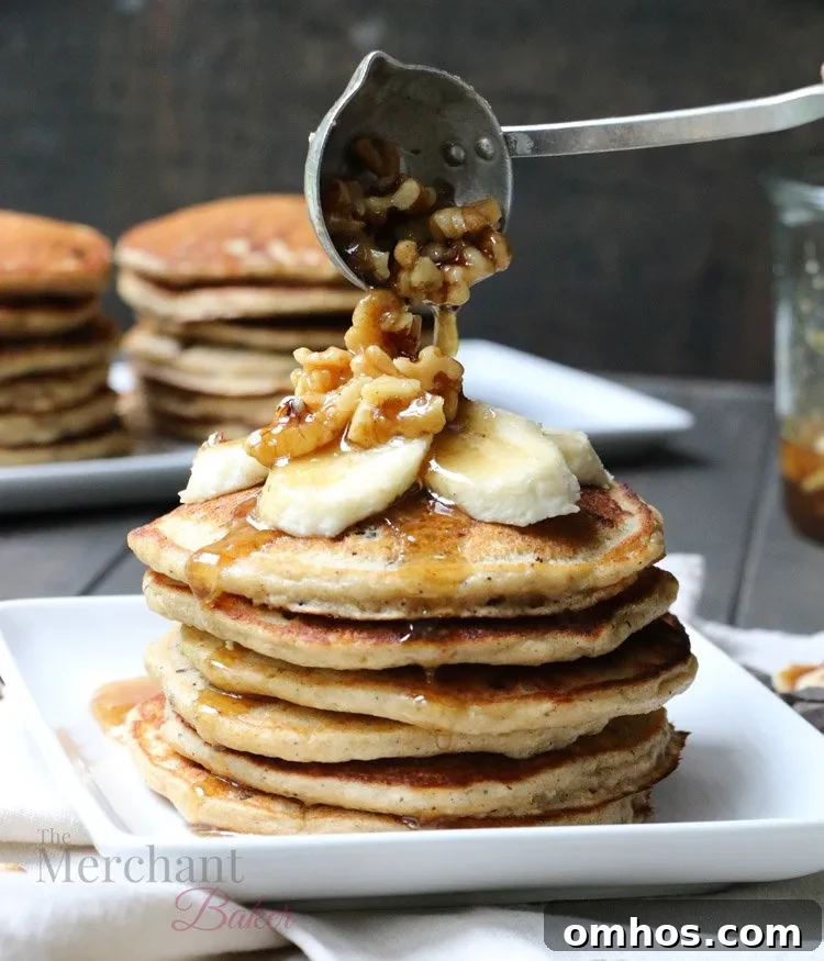 Walnut syrup being ladled over a stack of Oatmeal Chocolate Chip Banana Pancakes topped with sliced bananas