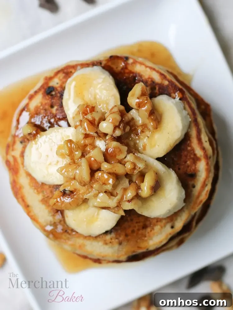 Overhead view of Stack of Oatmeal Chocolate Chip Banana Pancakes topped with sliced bananas and walnut syrup