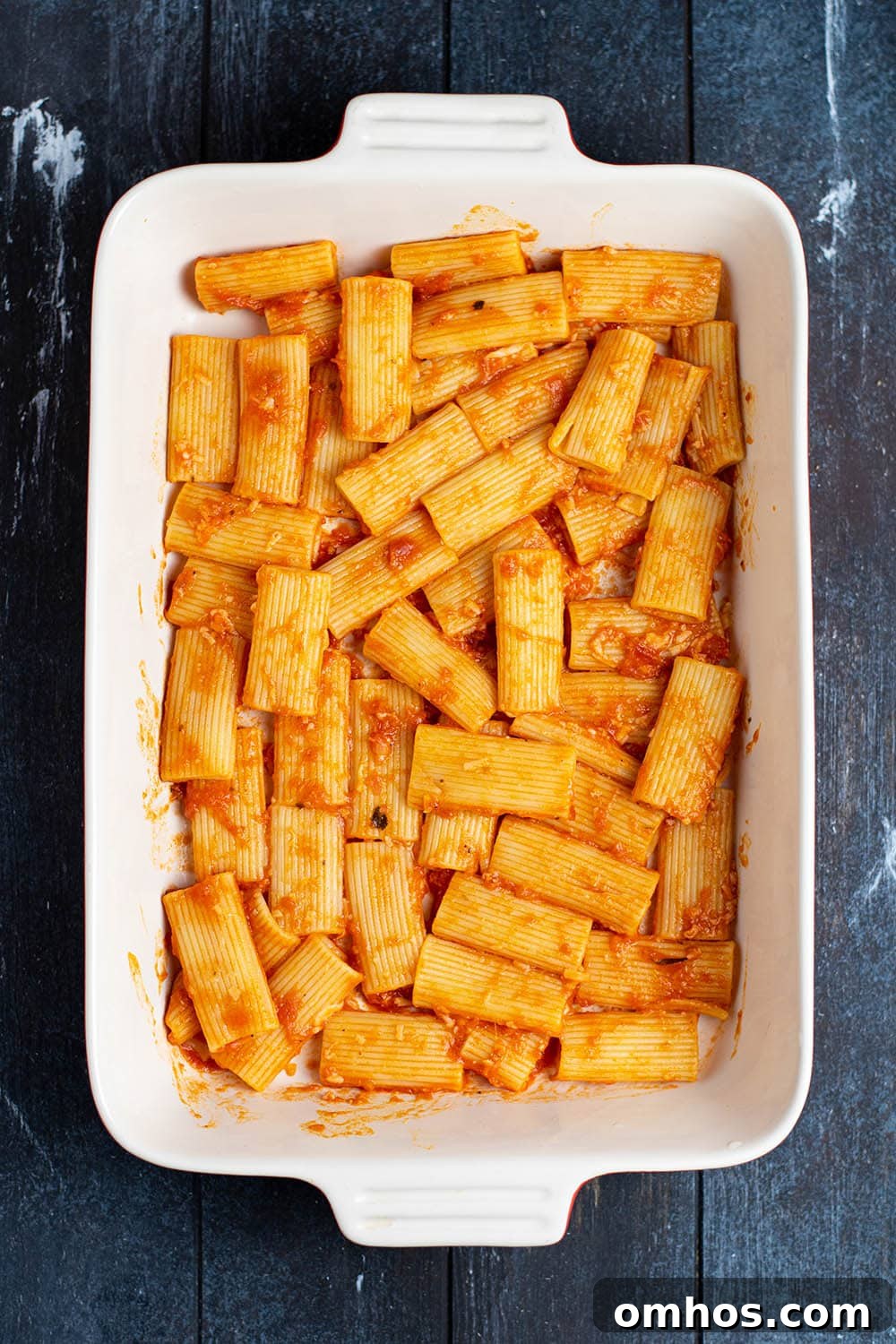 Rigatoni tossed with marinara in a white casserole dish.