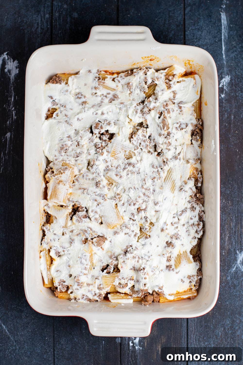 A layer of ricotta cheese on top of ground sausage and beef and rigatoni coated in marinara.