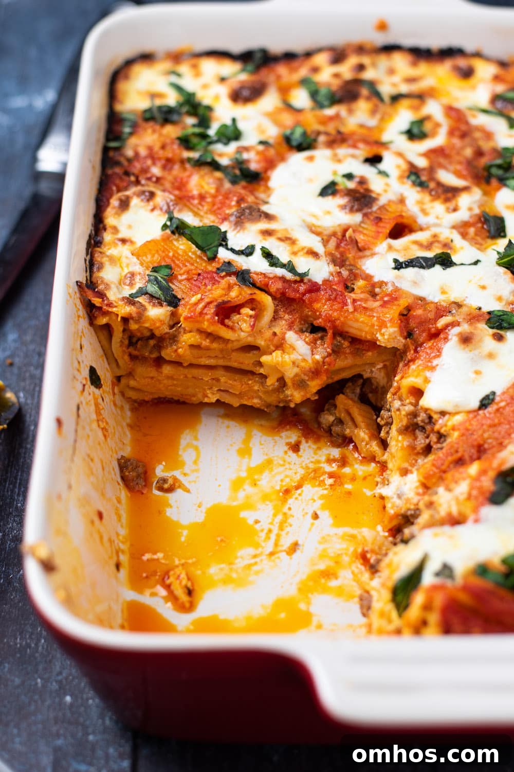 Golden baked rigatoni in a white casserole dish after a square slice has been removed.
