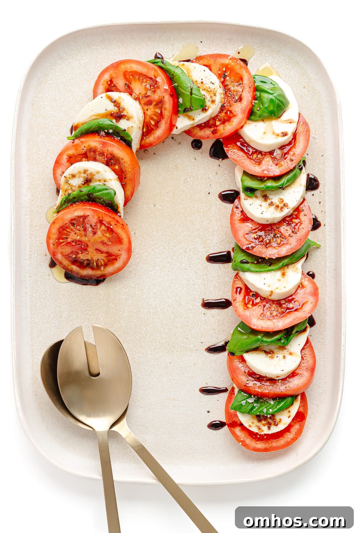Caprese salad arranged in the shape of a candy cane on a cream colored platter with salad servers.