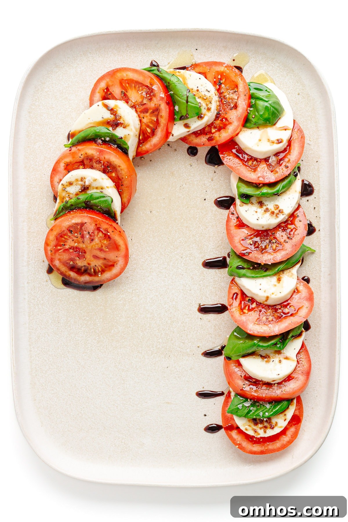 A Christmas caprese salad arranged in the shape of a candy cane on a cream colored rectangular serving platter.
