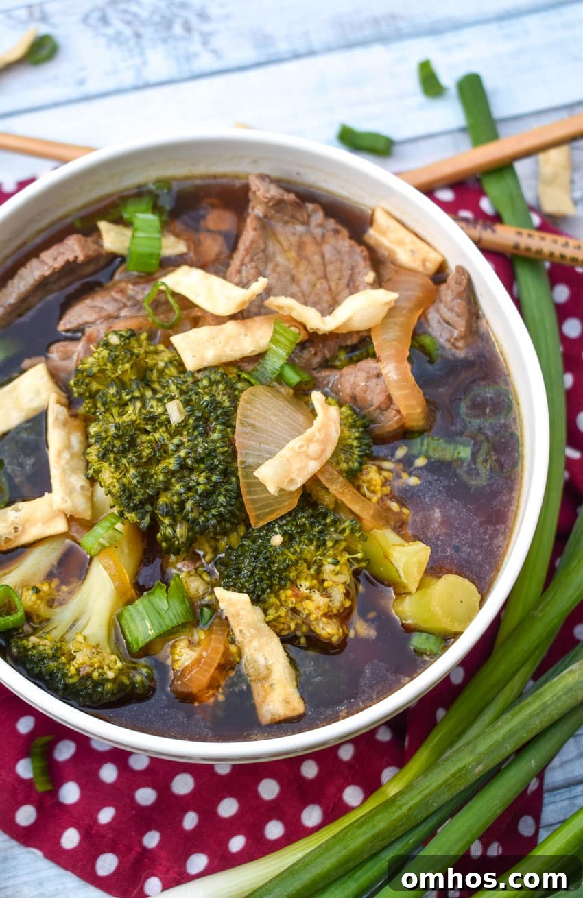 chinese beef and broccoli soup in a white bowl topped with crispy wonton strips and sliced green onions