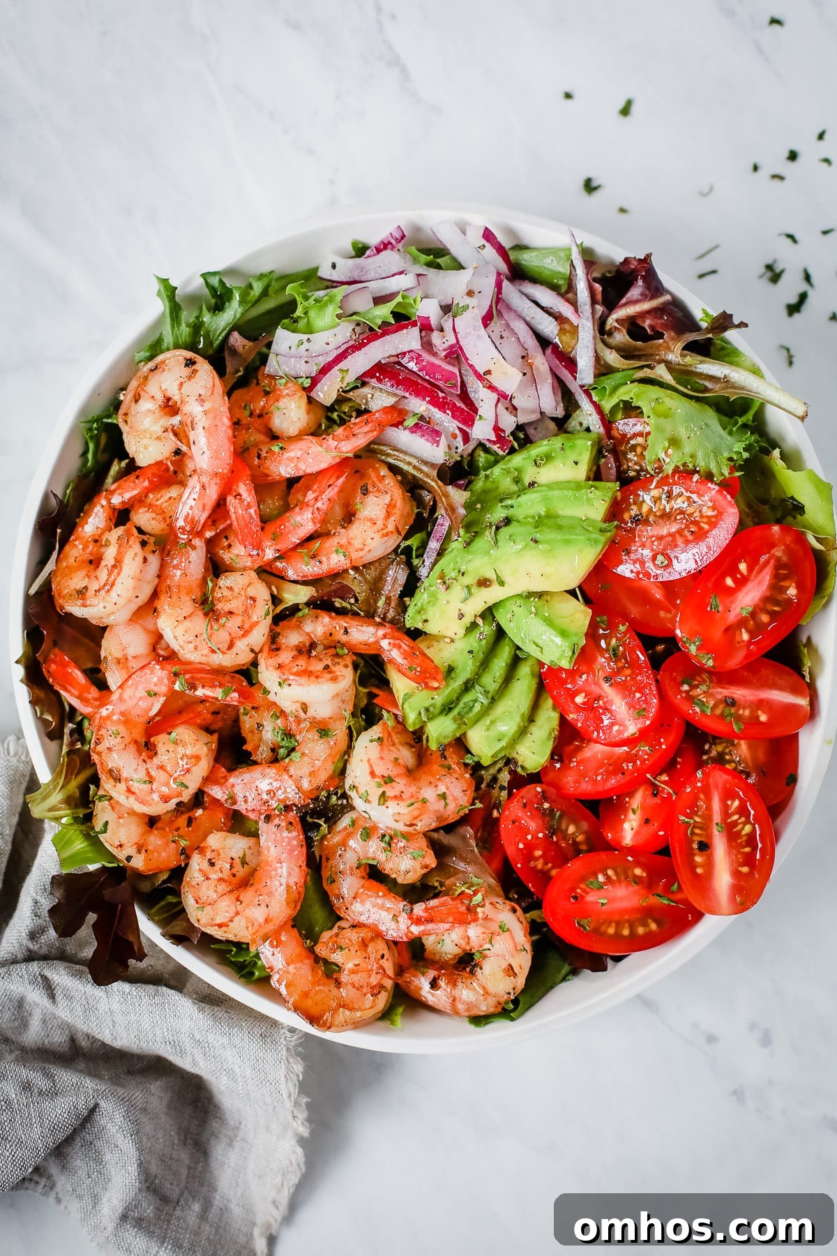 A bowl with shrimp, tomatoes, avocados, onions, and greens.