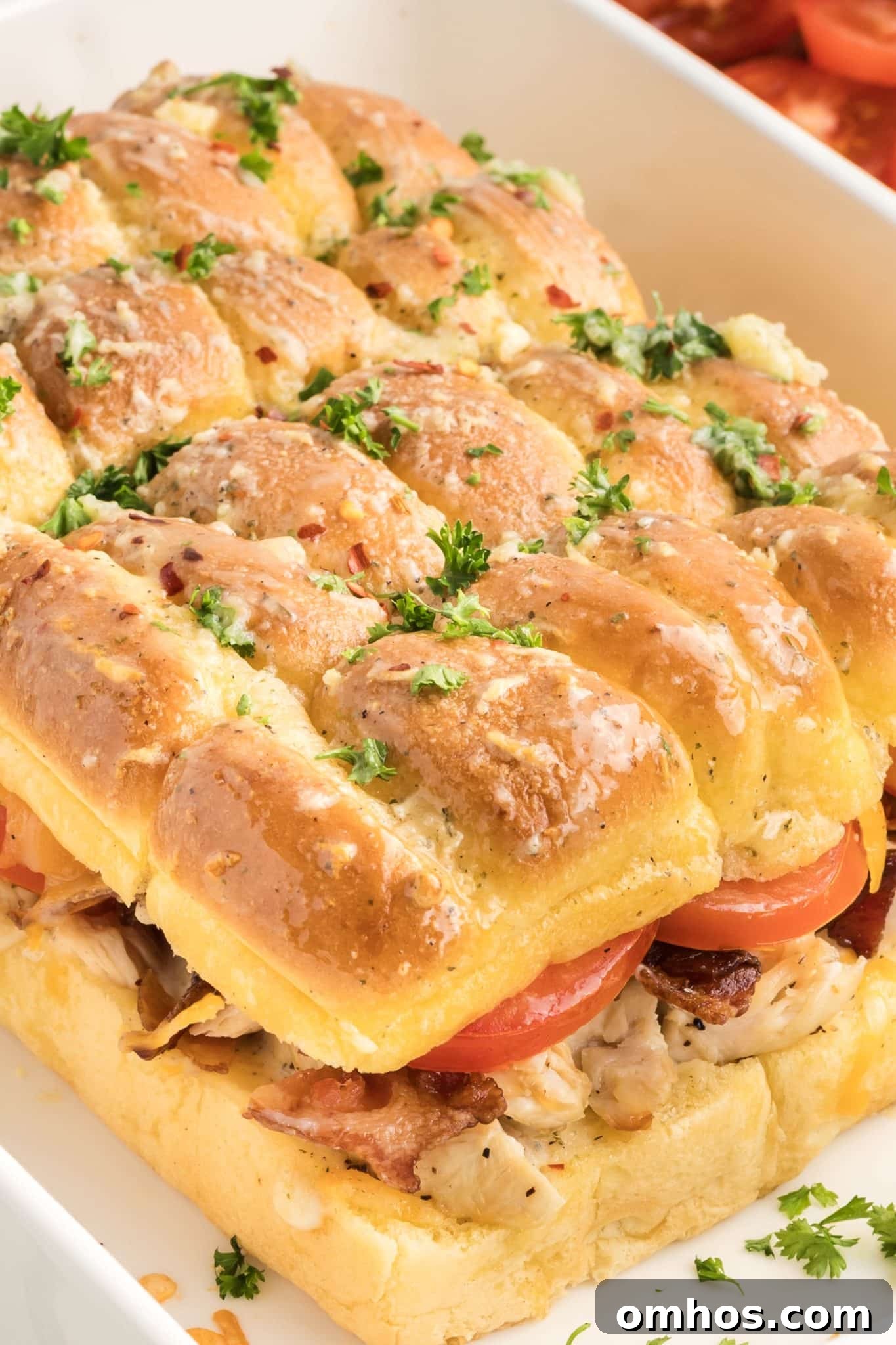 Sideview of a bacon ranch chicken sliders showing layers of melted cheese, bacon, chicken, and tomato with visible garlic butter on golden top bun.