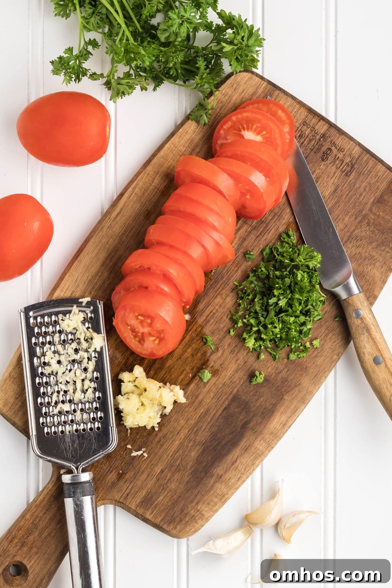 Sliced tomatoes, chopped parsley, and grated garlic on a cutting board.