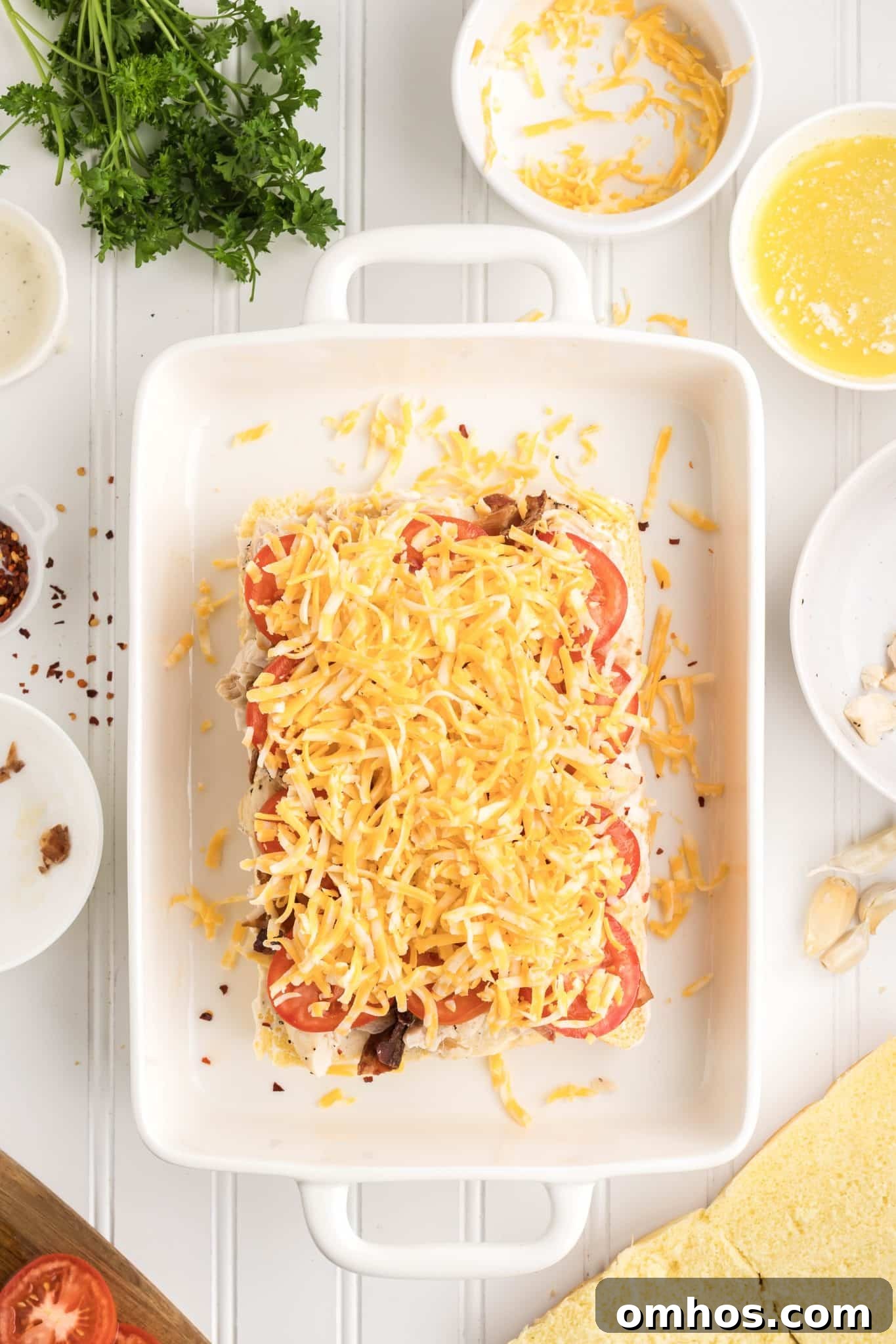 Shredded Colby-Jack cheese being sprinkled over chicken and bacon filled slider rolls before adding top buns.