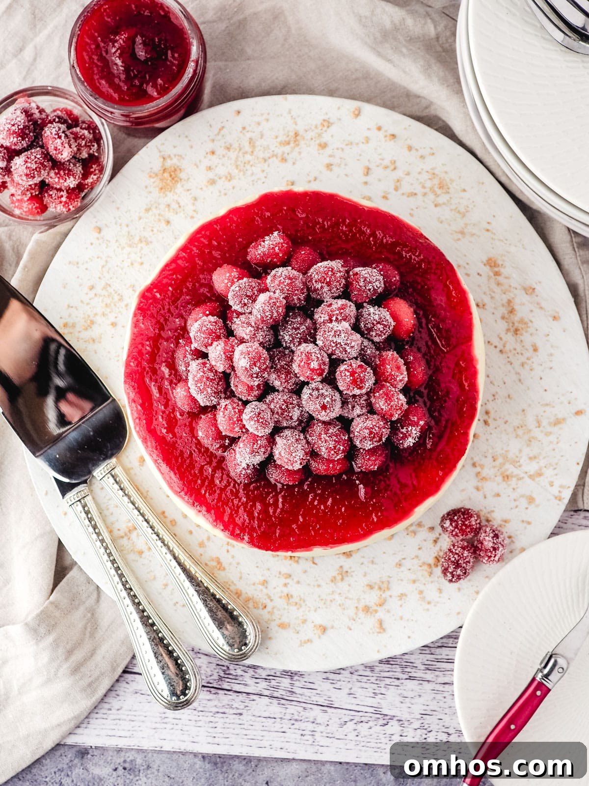 Serving sugared cranberries piled on top of a cranberry cheesecake with cranberry sauce, with serving wear on the side.